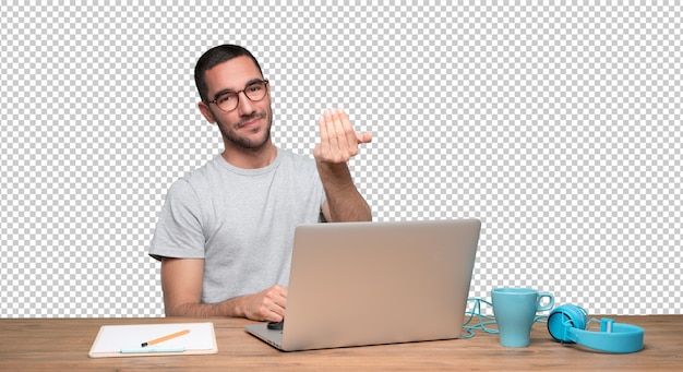 Confident young man sitting at his desk and doing a gesture of inviting with his hand