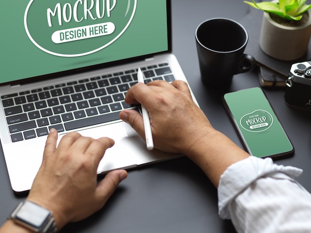 Cropped shot of male hands typing on laptop keyboard with mock up smartphone on black table