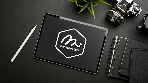 Dark creative workspace with tablet mockup, camera, stationery and stylus pen, top view