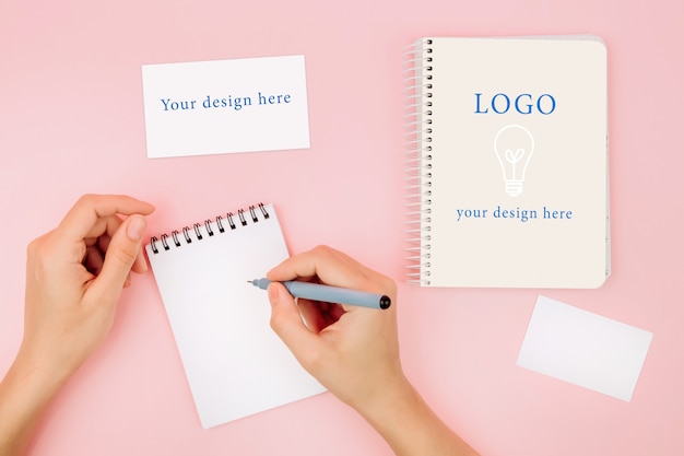 Female hands in a white shirt hold a notebook on a pink background, mockup