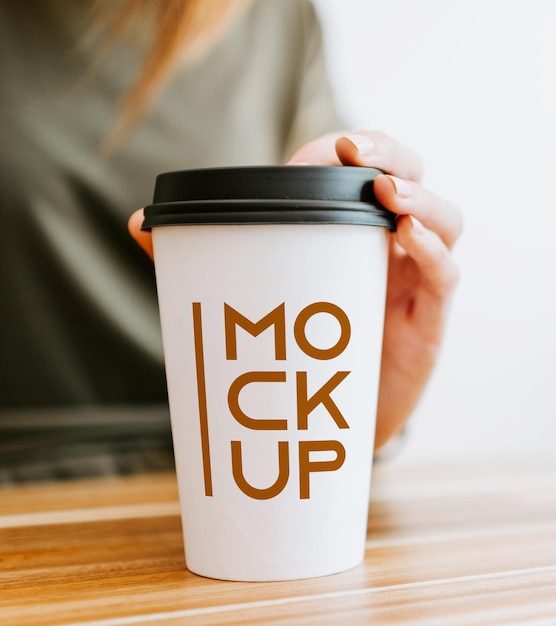 Free PSD mockup of a white disposable coffee cup in hand on table