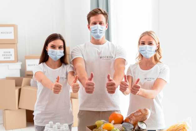 Front view of volunteers with medical masks giving thumbs up