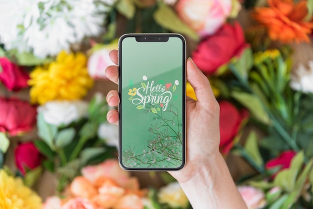 Hand holding smartphone mockup above flowers