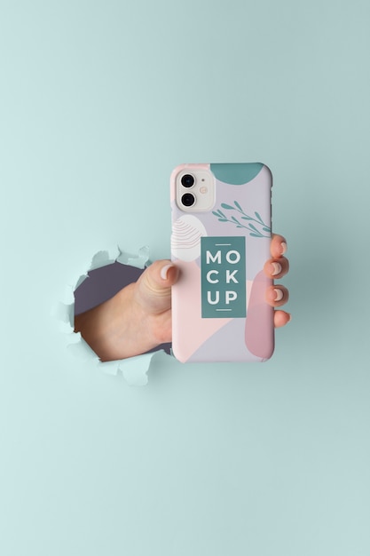 Hand holding smartphone with mock-up phone case through wall tear