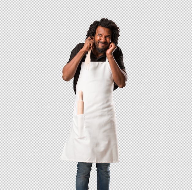 PSD handsome african american baker covering ears with hands, angry and tired of hearing some sound