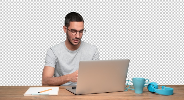 Happy young man sitting at his desk and using his laptop