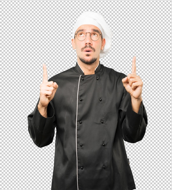 PSD hesitant young chef pointing up with his finger