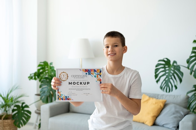 PSD little boy at home holding a certificate mock-up