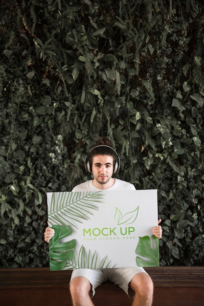 Man presenting poster mockup in front of leaves