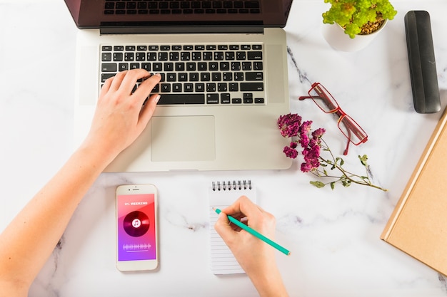 Mockup of hand writing on notepad with laptop and smartphone