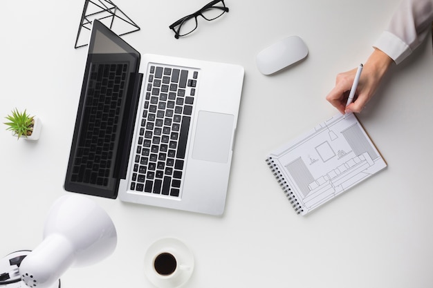 Office desk with laptop and man writing on notebook mock-up