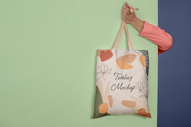 Person holding tote bag mock-up behind wall