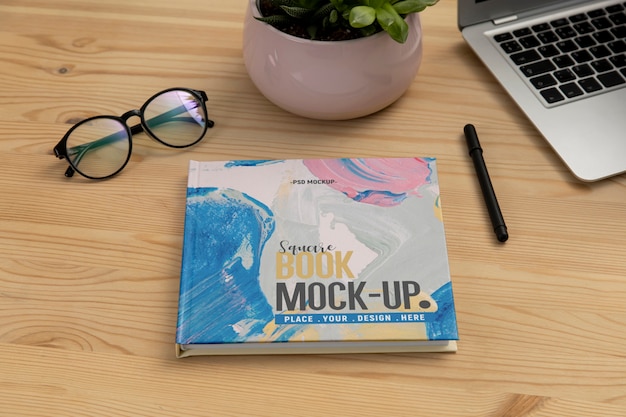 Square book mock-up on wooden office desk with laptop and eyeglasses