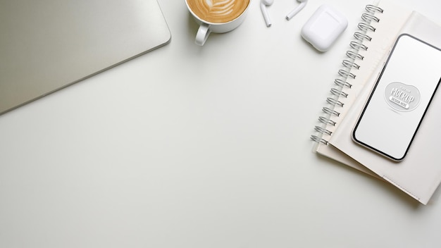 Top view of creative desk with smartphone mockup, notebooks, laptop and supplies