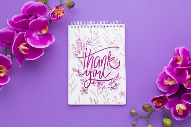 Top view of notebook and flowers on purple background