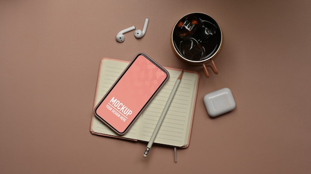 Top view of workspace with smartphone mockup, accessories on notebook and coffee cup