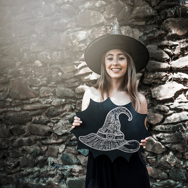 Woman dressed as a witch holding a sketch of a hat