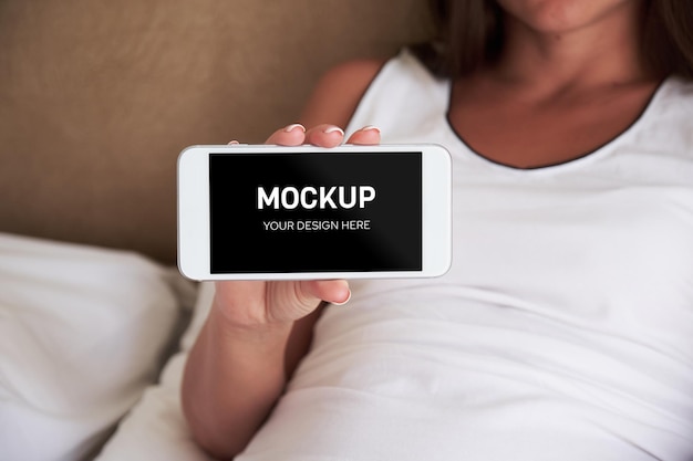 A woman shows the screen of the phone to the camera while lying on the bed Smartphone mockup