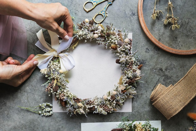 PSD woman tying a ribbon on a floral wreath  over a white card mockup