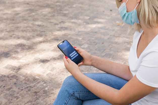 Woman wearing mask on street reading book  on phone