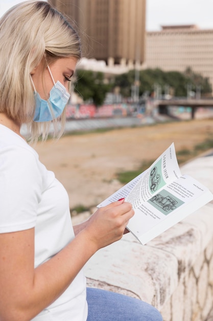 Woman with mask reading book on street