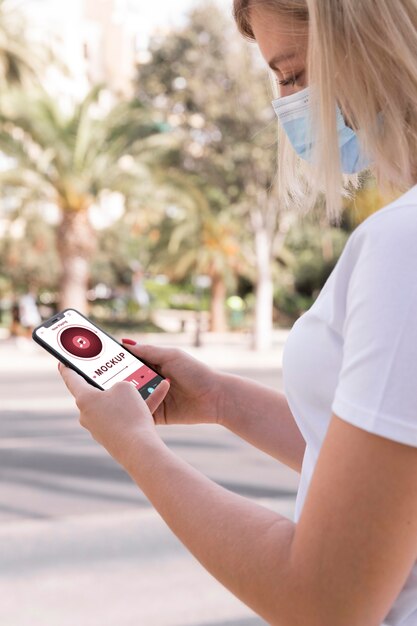 Woman with mask on street reading book on phone