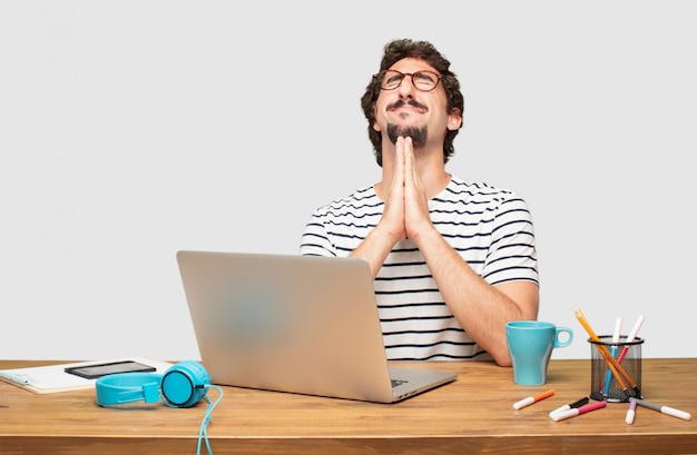 PSD young bearded graphic designer with a laptop praying in a saintly manner