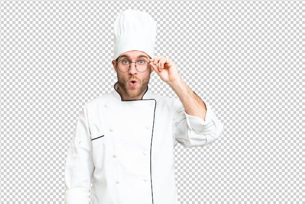 PSD young blonde man chef over isolated chroma key background with glasses and surprised