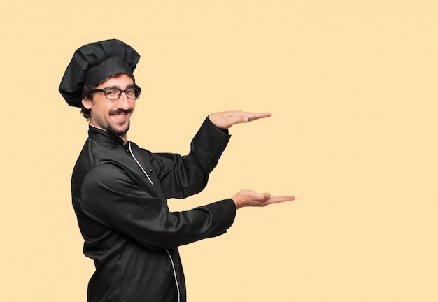 young crazy man as a chef smiling with a satisfied expression showing an object or concept