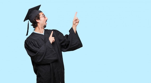 young graduated man smiling and pointing to the side with both hands