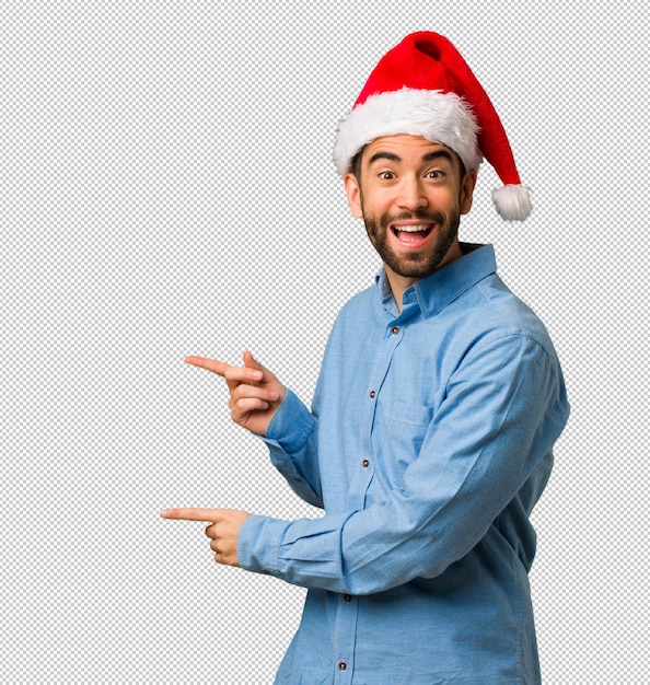 Young man wearing santa hat pointing to the side with finger