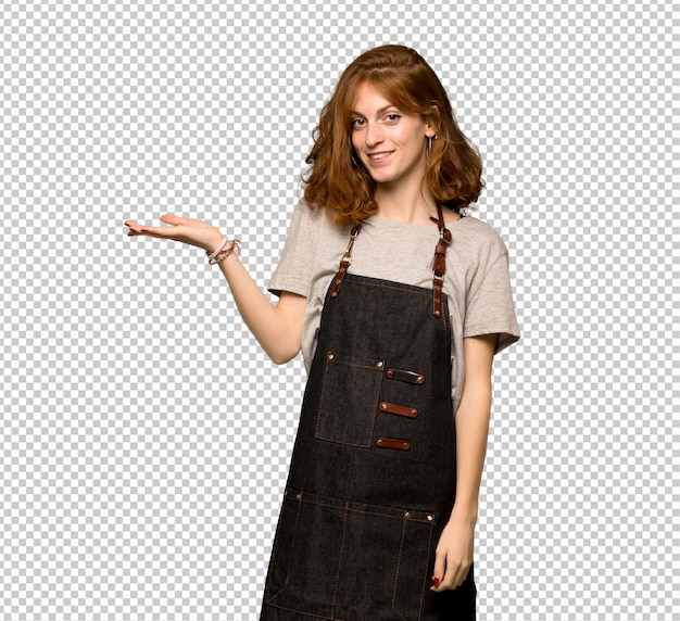 Young redhead woman with apron holding copyspace imaginary on the palm to insert an ad