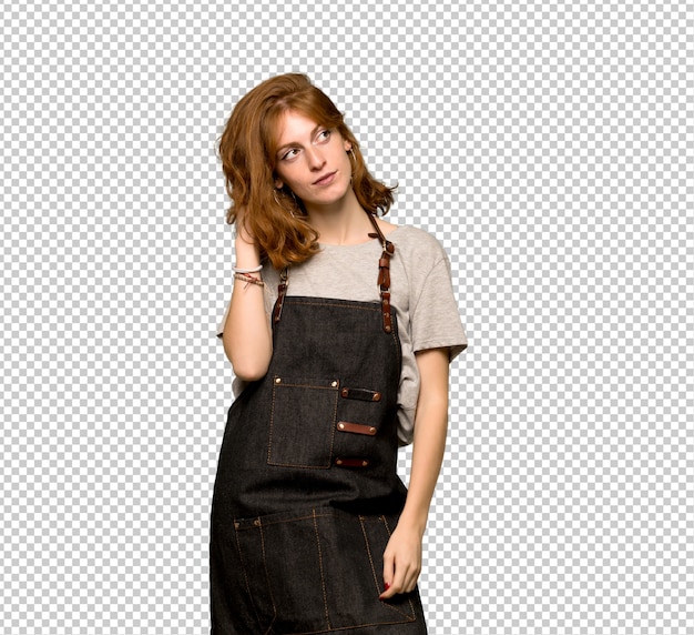 Young redhead woman with apron thinking an idea while scratching head