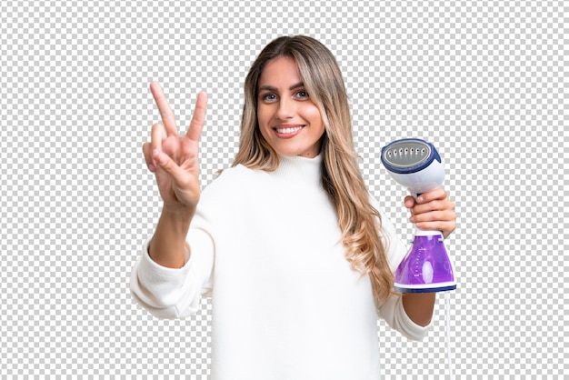 PSD young uruguayan woman holding an iron over isolated background smiling and showing victory sign