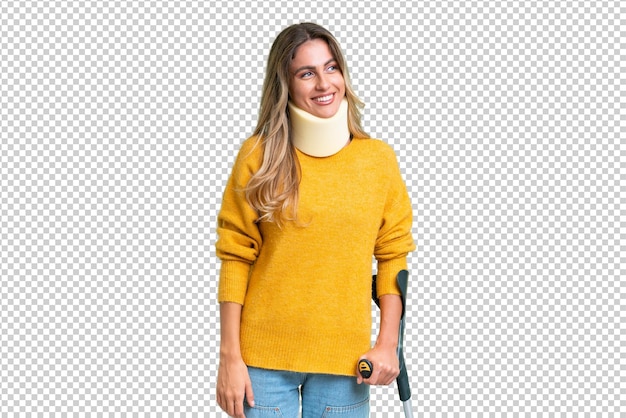 Young Uruguayan woman wearing neck brace and crutches over isolated background with happy expression