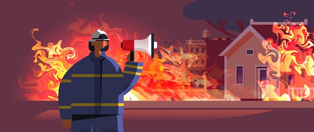 brave fireman holding loudspeaker firefighter in uniform and helmet firefighting emergency service extinguishing fire concept burning house exterior orange flame portrait