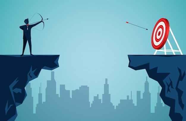 Businessman standing on cliff is shooting an arrow across the cliff opposite the arrow to the target in the center of the red circle