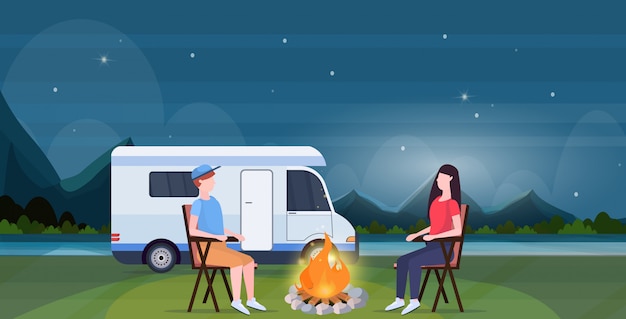 couple sitting around campfire at night near camping trailer truck caravan car man woman spendingtime togeher summer vacation concept beautful nature landscape background full length horizontal