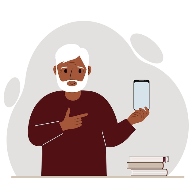 A happy grandfather holds a mobile phone in one hand and points at it with the index finger of his other hand.