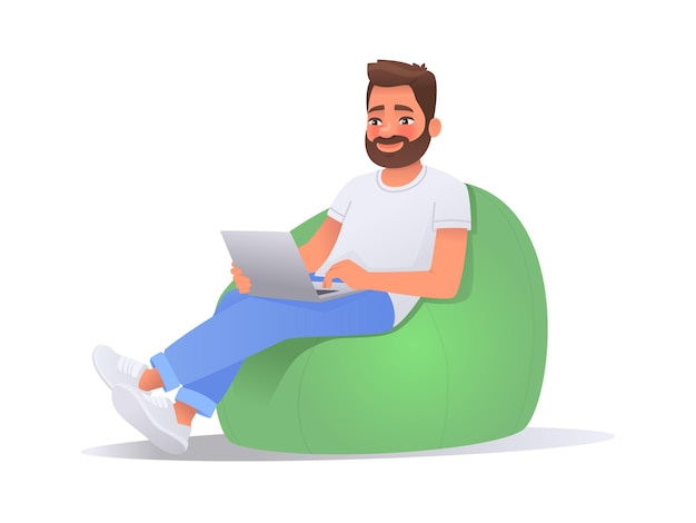 Happy man working on a laptop computer while sitting in a bean bag chair Freelancer guy working home