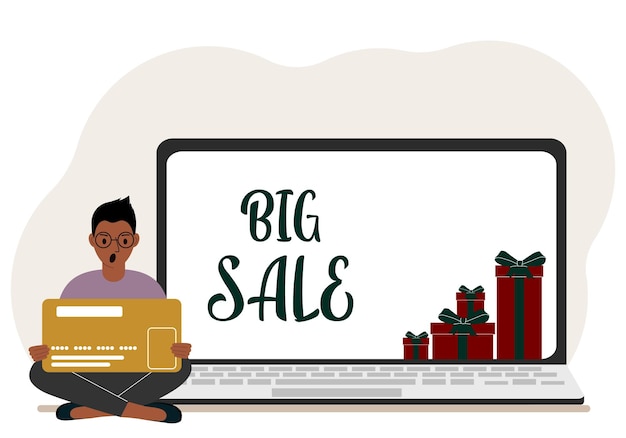 Online shopping Big sale A man sits crosslegged in his hands holding a shopping card Next to a laptop with gifts