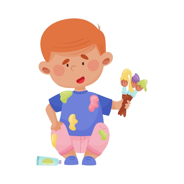 Playful boy in stained clothes sitting and holding paintbrushes and paints vector illustration