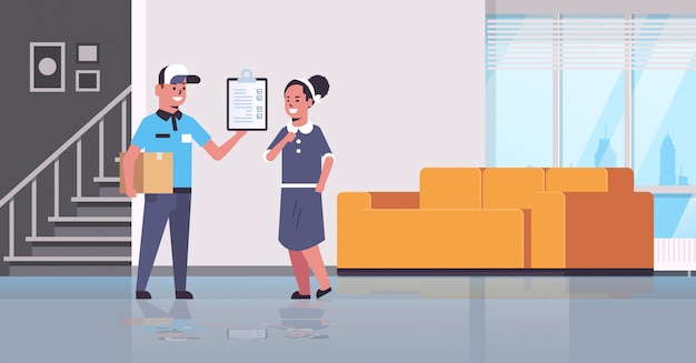 postman in uniform holding cardboard parcel box courier showing clipboard to woman recipient express delivery service concept modern living room interior 